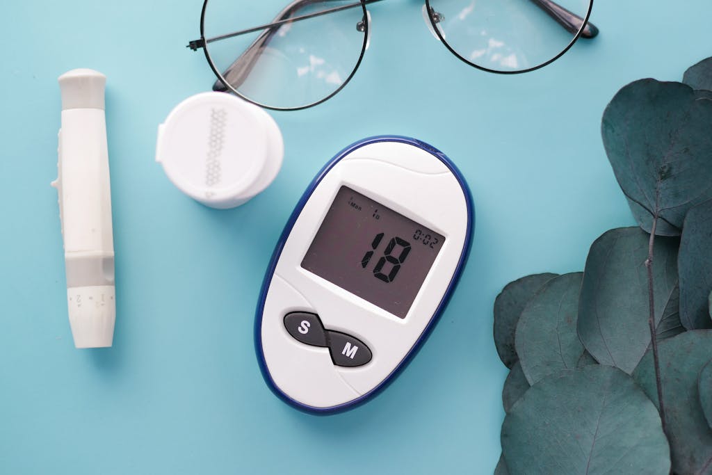 A top view of a glucometer, test strip, and glasses on a blue background, symbolizing health management.