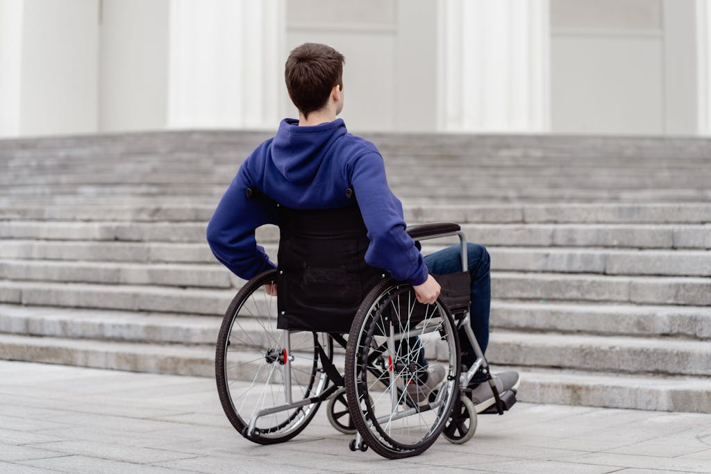 Back view of a young man in a wheelchair facing steps in a city setting.